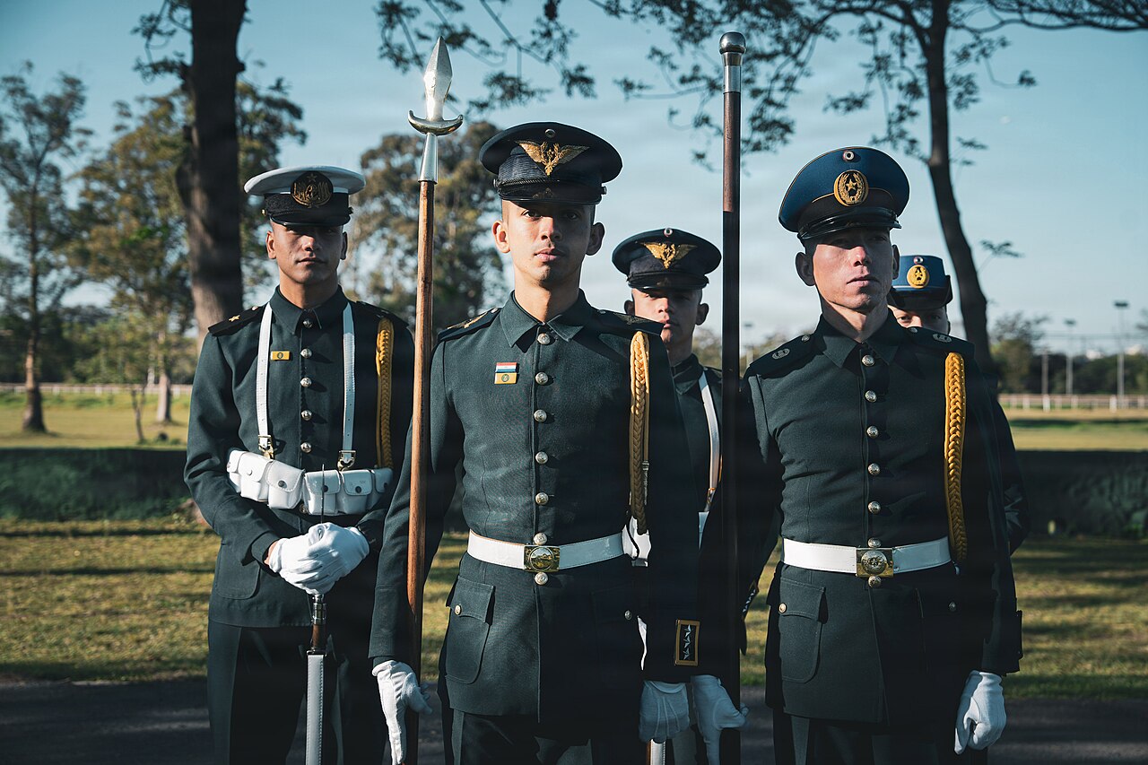 Members of the Paraguayan military color guard in dark green dress uniforms and white gloves stand at attention outdoors
