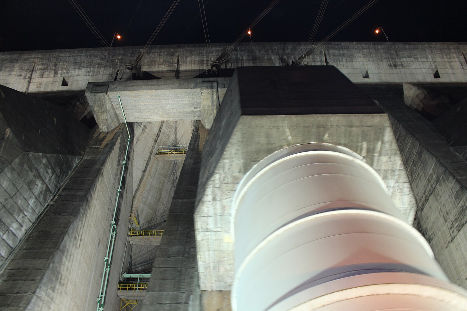 Concrete wall and a steel penstock pipe of the Itaipú hydroelectric dam seen from below at night