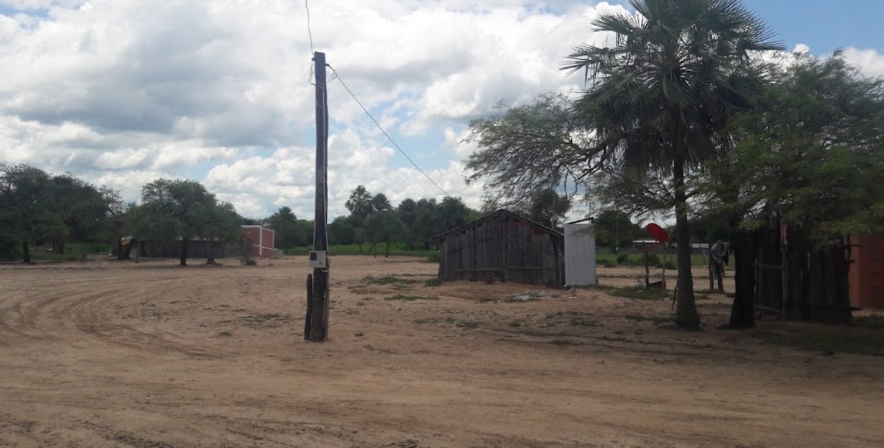 A sandy street with wooden huts and palm trees in Misión San Leonardo, an indigenous community in the Paraguayan Chaco