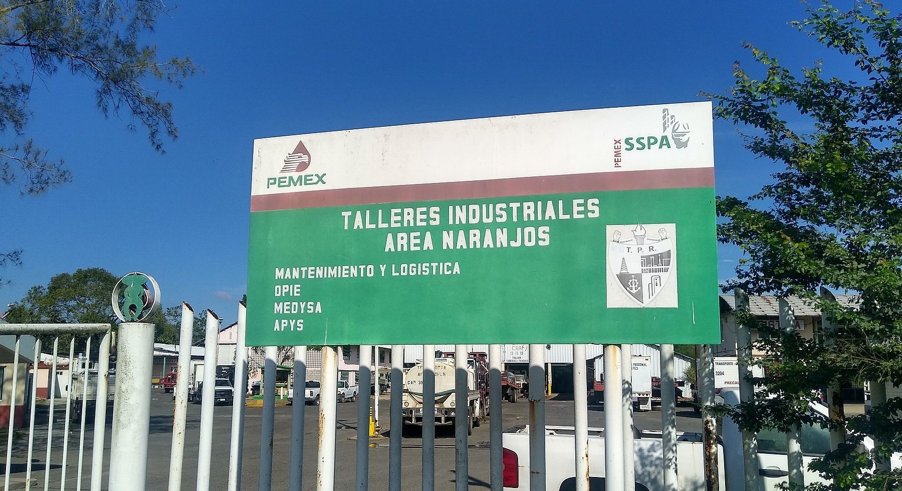 A Pemex industrial workshops site sign at Naranjos, Veracruz, with company logos and parked trucks behind a gate