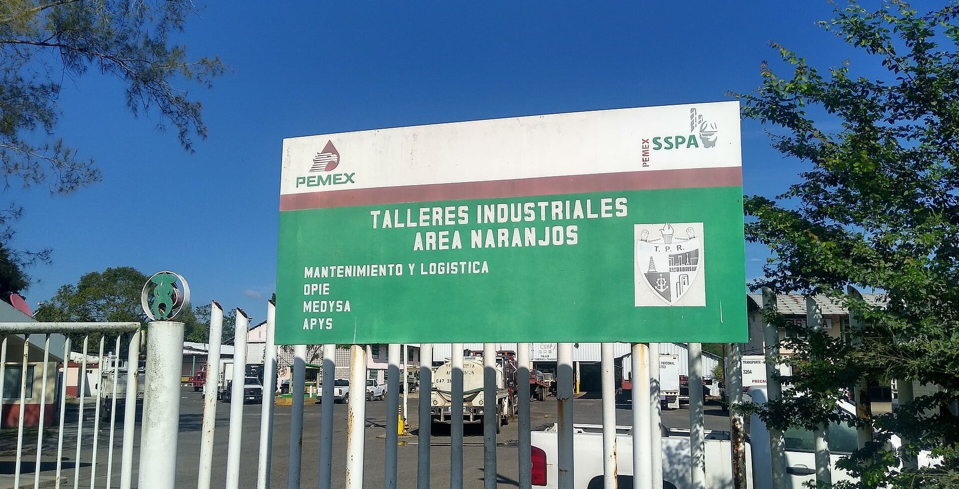A Pemex industrial workshops site sign at Naranjos, Veracruz, with company logos and parked trucks behind a gate
