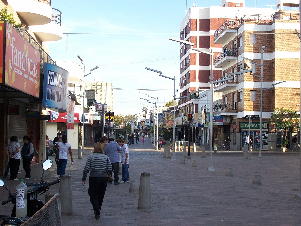 Pedestrian shopping street with shops, a pharmacy, brick apartment blocks and people walking in central Florencio Varela
