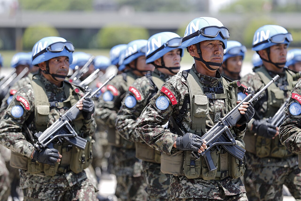 Peruvian soldiers in camouflage and blue United Nations helmets marching with rifles