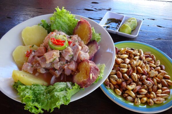 A plate of trout ceviche with sweet potato, boiled potato and toasted corn kernels on a dark wooden table