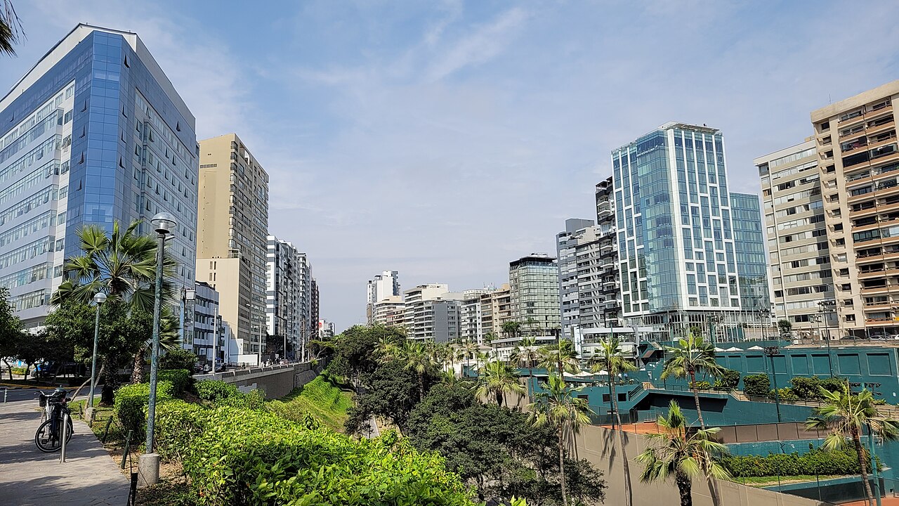Glass and concrete towers above green slopes and palm trees in the Miraflores district of Lima