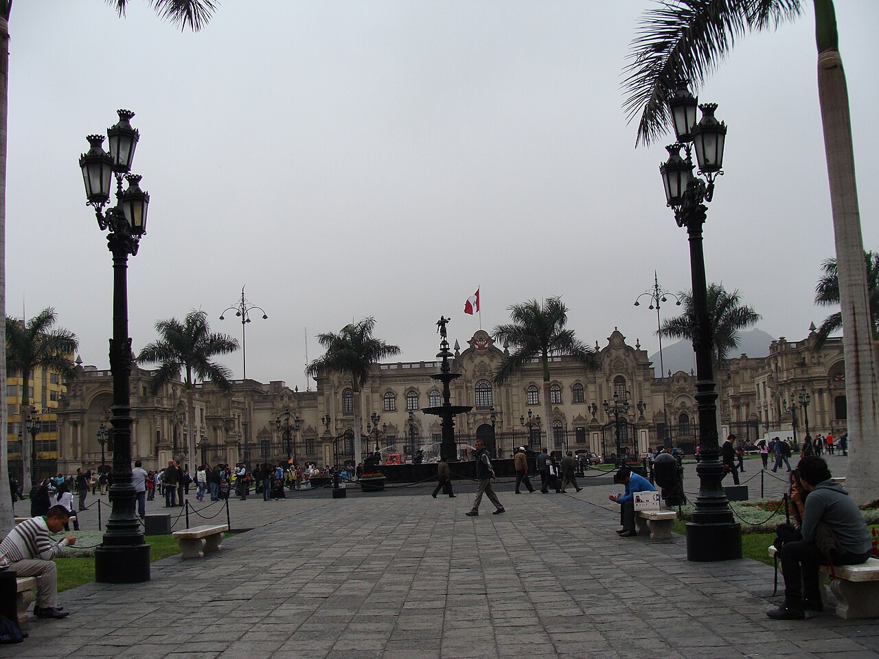 Government Palace on Plaza Mayor in Lima, Peru, with a Peruvian flag above the building and people crossing the square