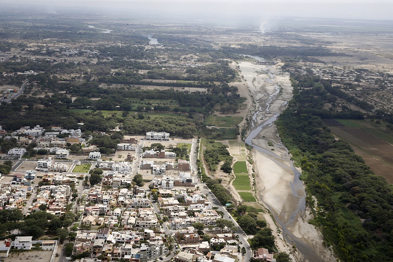 Aerial view of homes beside the Piura River in northern Peru, with a mostly dry riverbed and farmland