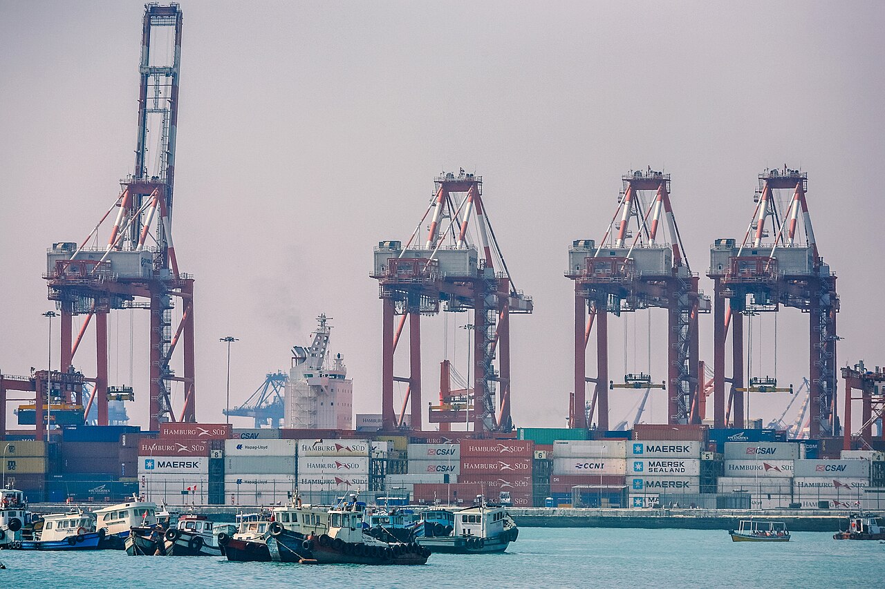 Container cranes and stacked shipping containers at the port of Callao, with tugboats in the foreground