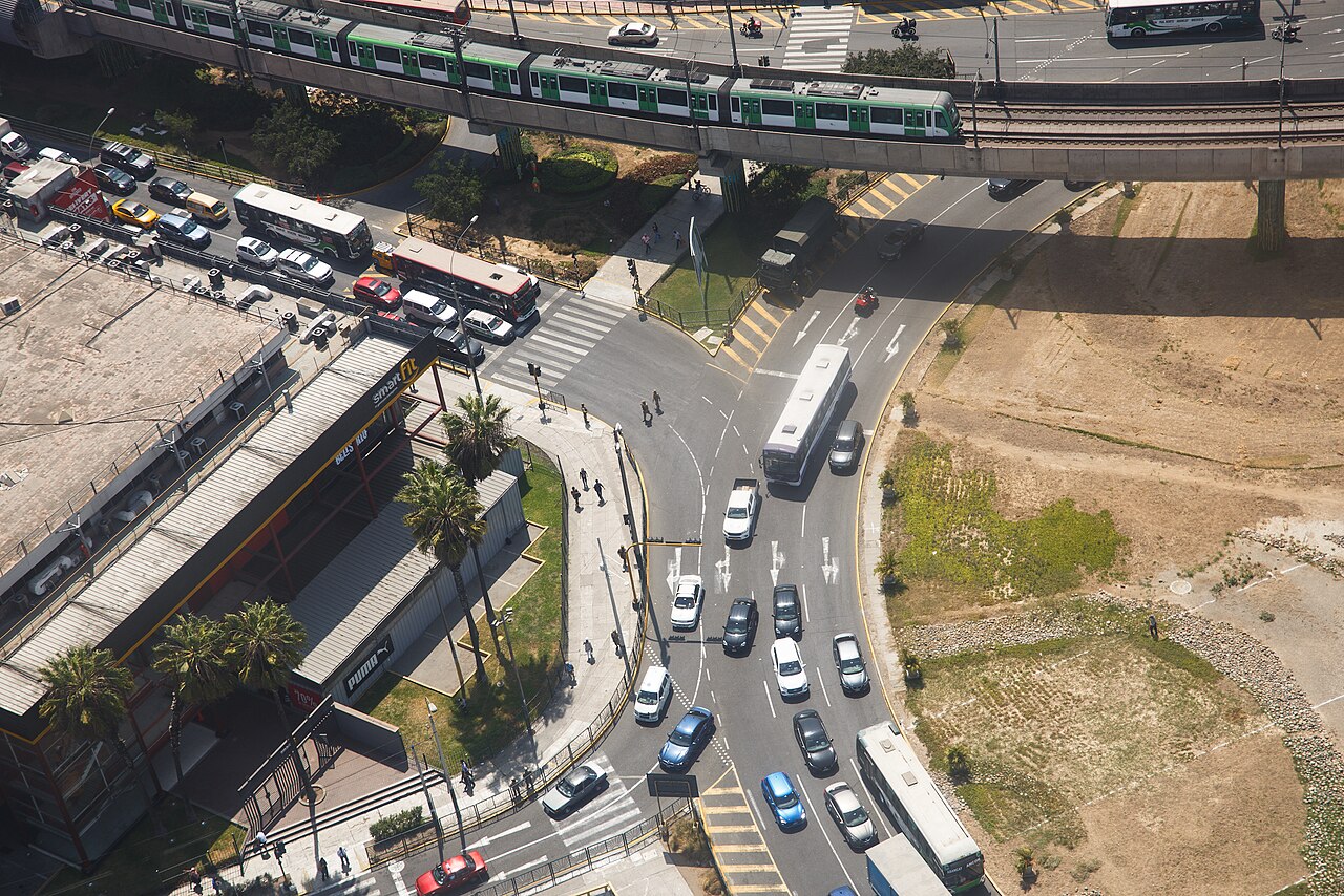 Aerial view of buses and cars at a Lima intersection beneath an elevated Metro Line 1 train