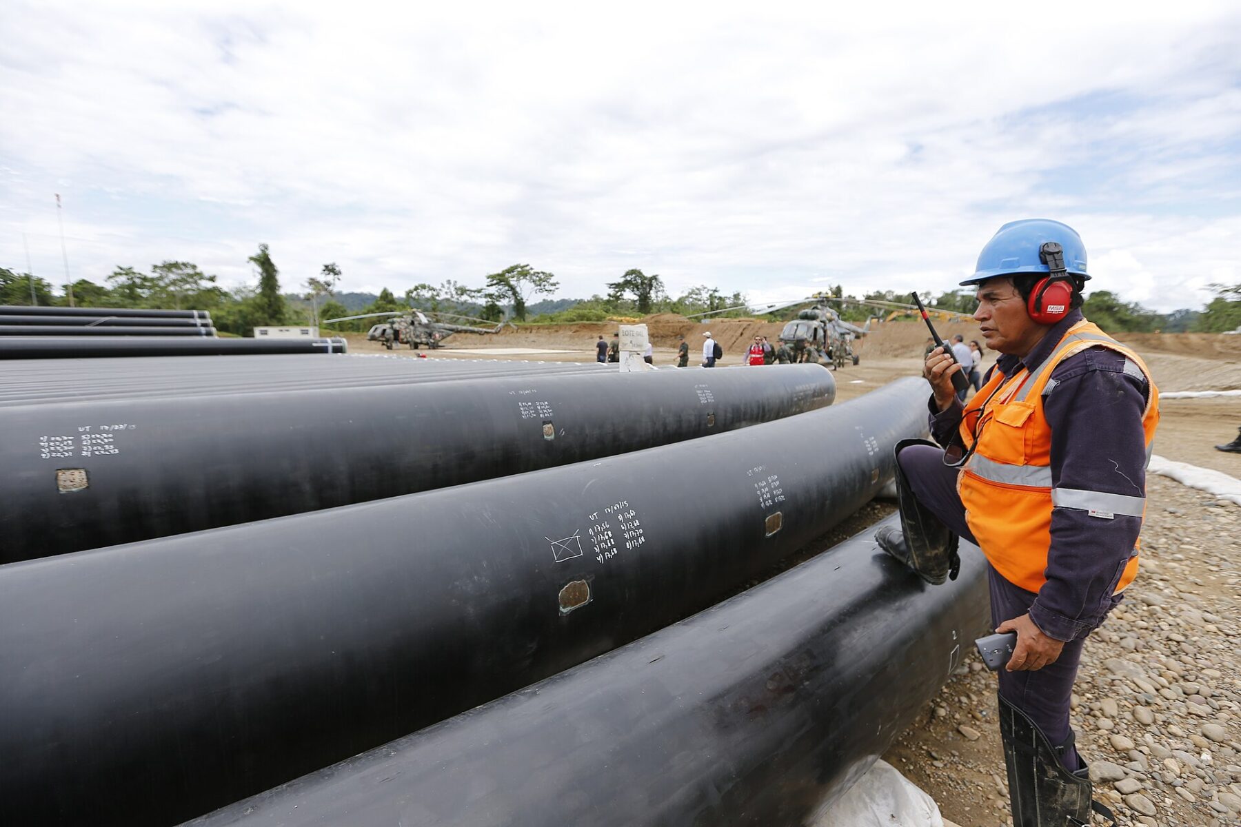 Steel pipe sections beside a worker at an energy corridor site in La Convención, Cusco, Peru