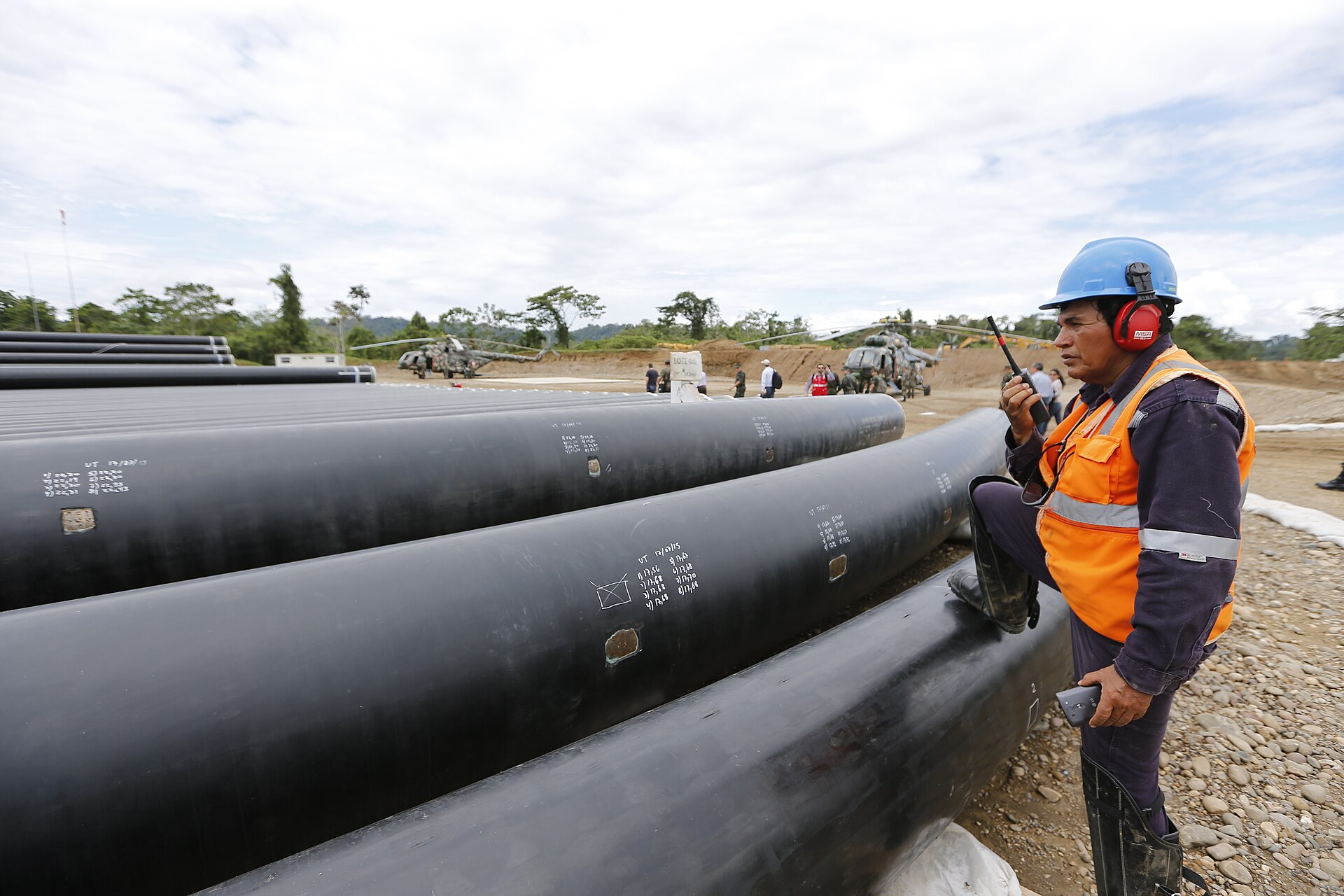 Steel pipe sections beside a worker at an energy corridor site in La Convención, Cusco, Peru