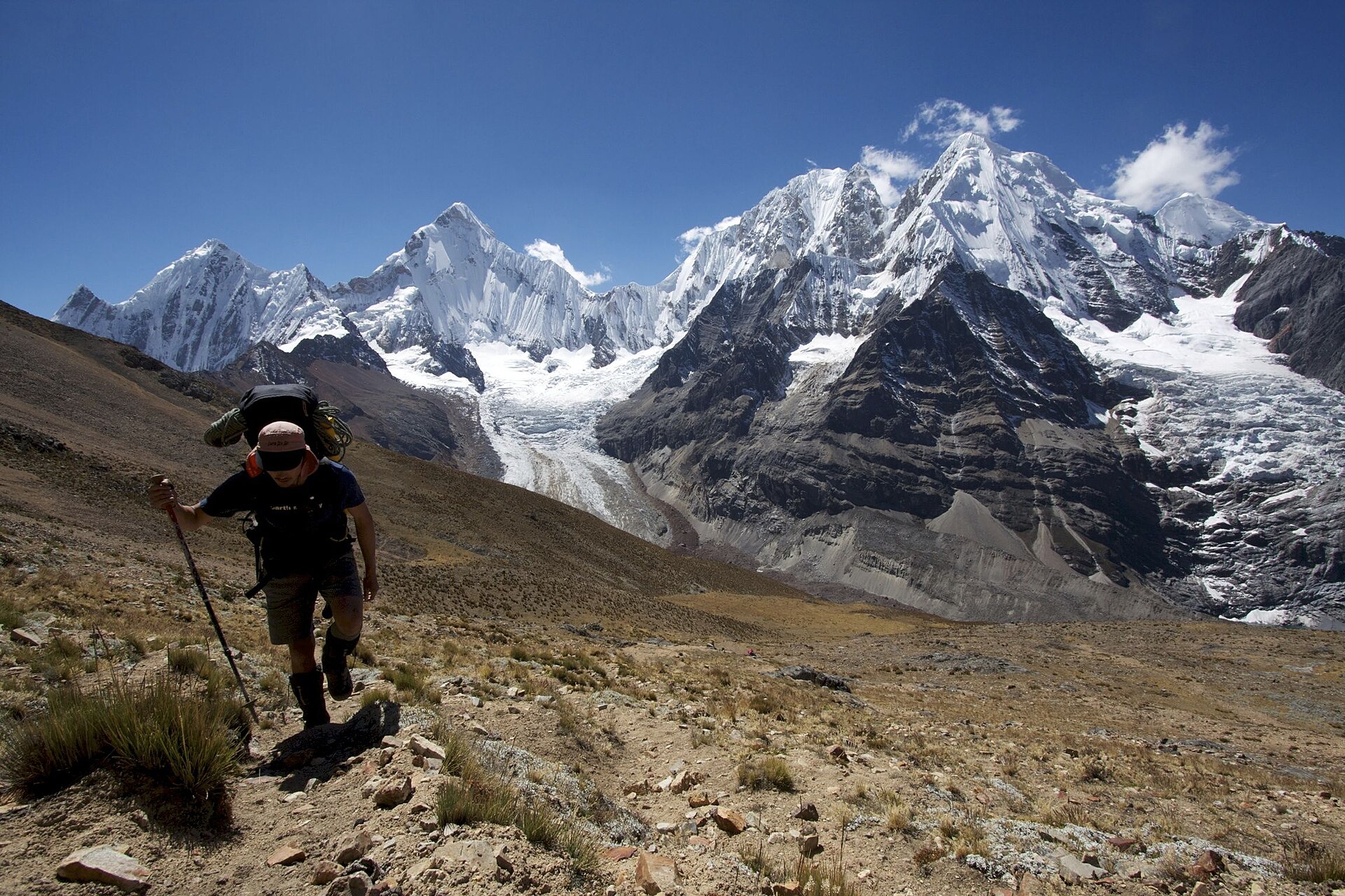 A trekker climbs a trail in the Cordillera Huayhuash with Yerupajá and Siula Grande behind