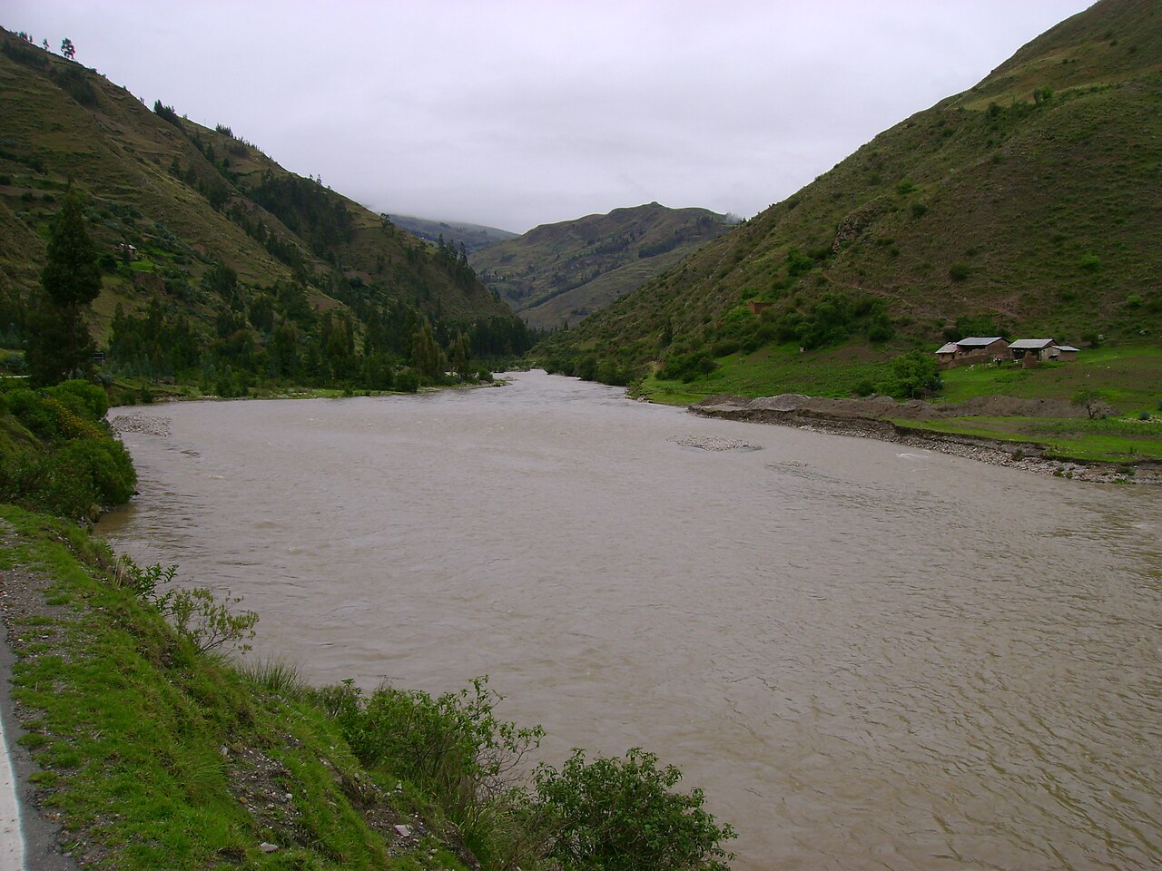 Muddy Marañón River winding through a green Andean valley with a few farm buildings on the right bank