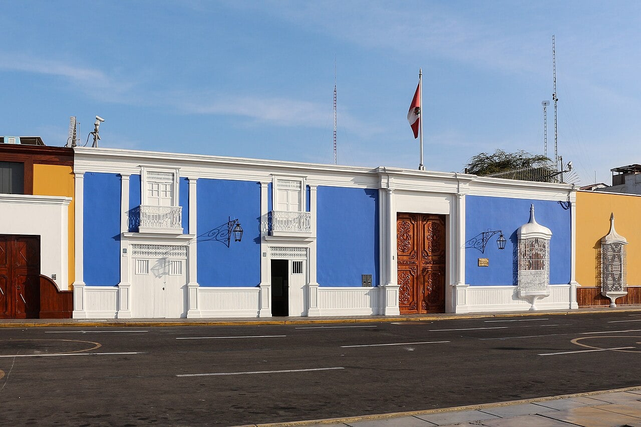 Blue and white colonial facade of the Central Reserve Bank of Peru branch in Trujillo, with carved wooden doors and a Peruvian flag on the roof