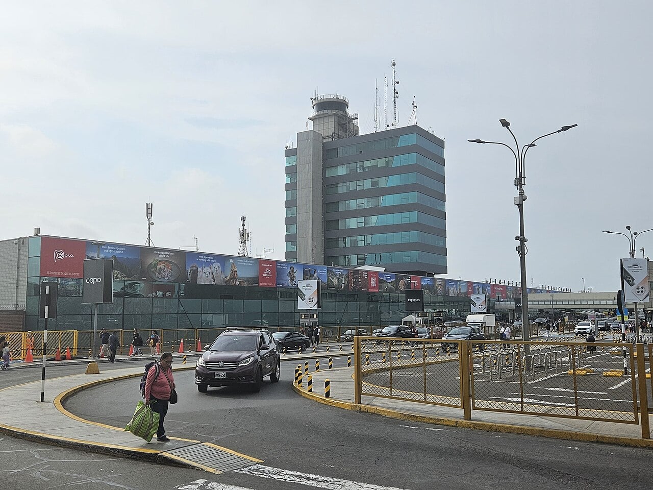 Control tower and former terminal entrance of Jorge Chávez International Airport in Lima, with cars and a pedestrian in the foreground