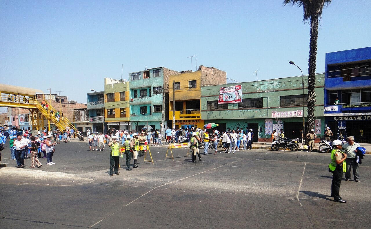 Traffic police officers in yellow vests stand on a wide road beside the Panamericana Norte in Lima, with pedestrians, a footbridge and colourful buildings behind