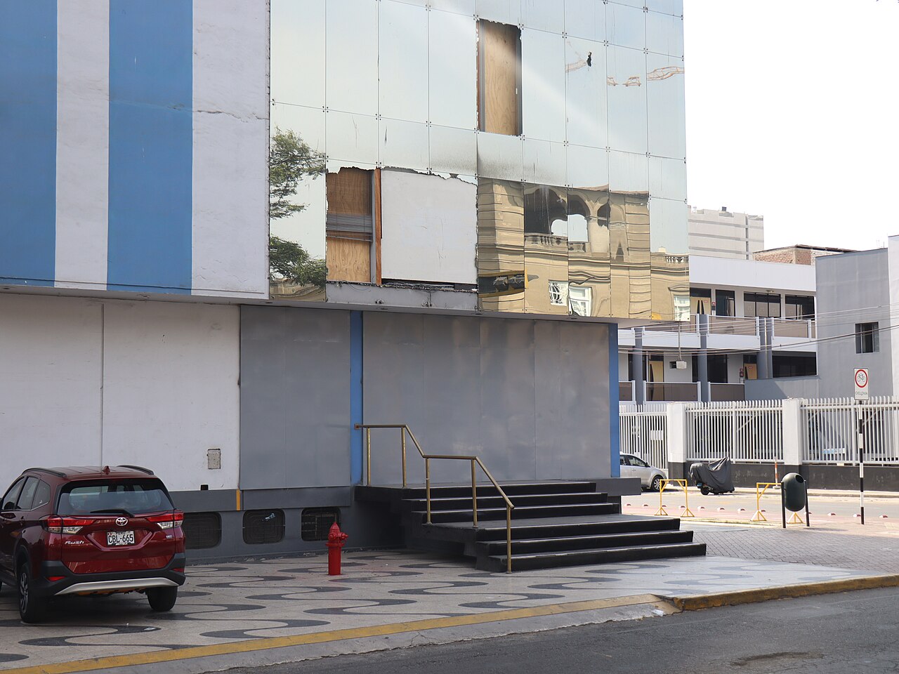 The worn blue-and-white facade of the Panamericana Televisión building on Avenida Arequipa in Lima, with several mirrored panels missing and boarded up.