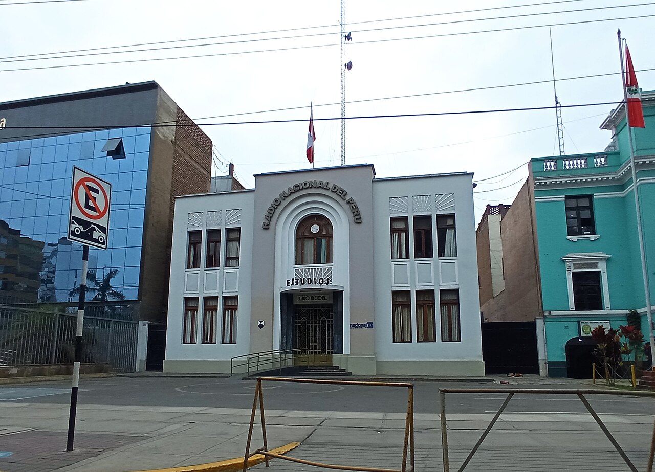 The white art deco headquarters of Radio Nacional del Perú in Lima, with the station name above an arched entrance and a Peruvian flag on the roof.
