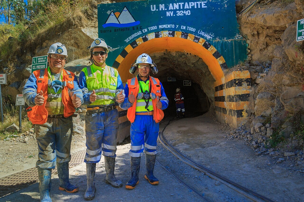 Three miners in helmets and high-visibility vests at the entrance of the Antapite underground gold mine in southern Peru