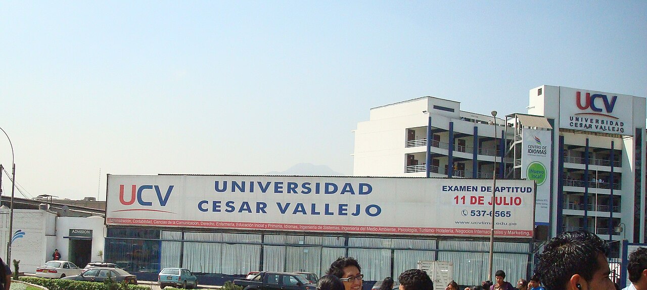 A white university building with a large blue and red UCV Universidad César Vallejo sign above a covered entrance, with students in the foreground
