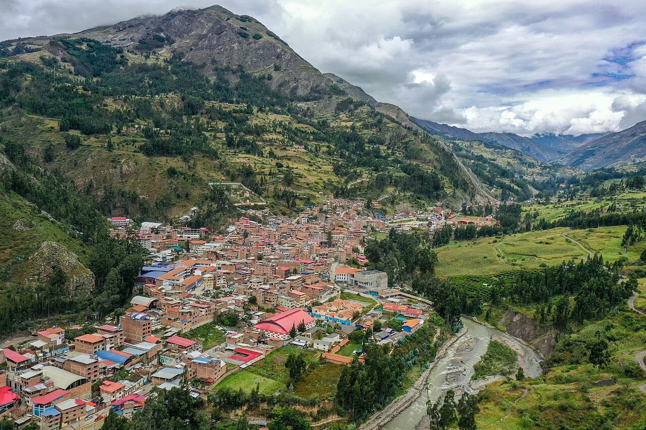 Aerial view of the town of San Marcos in a green Andean valley, with red-roofed buildings beside a river and mountains behind