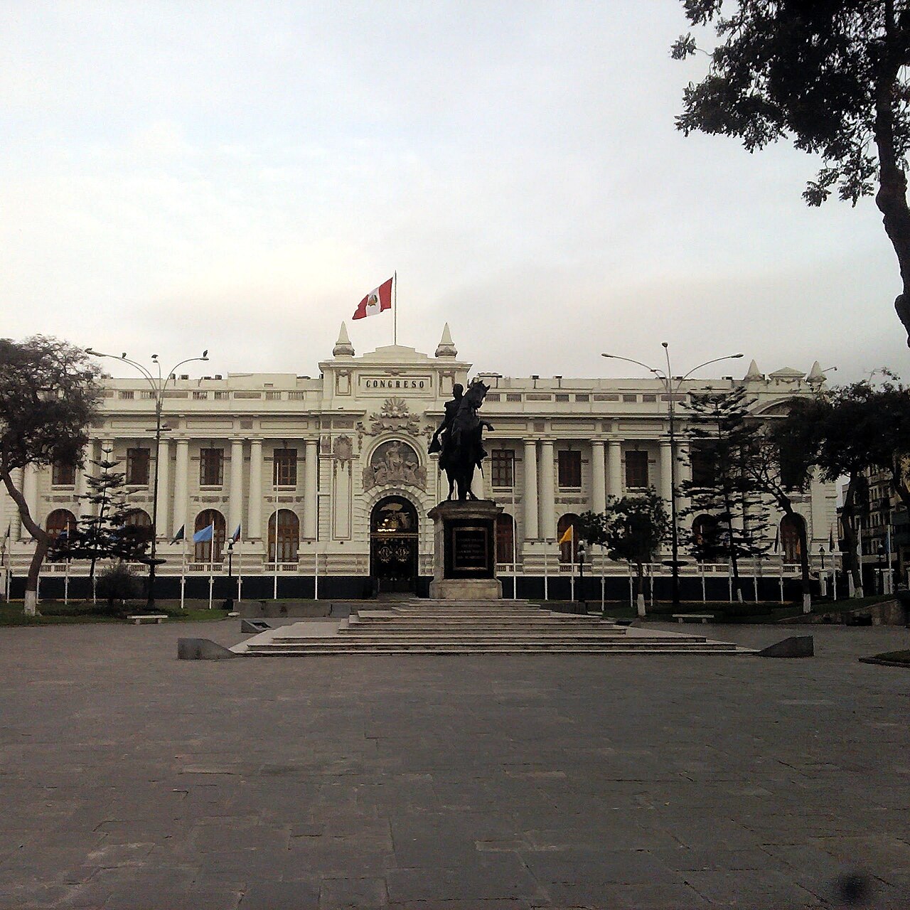The Congress building in Lima behind the Bolívar statue, with a Peruvian flag flying on the roof at dusk