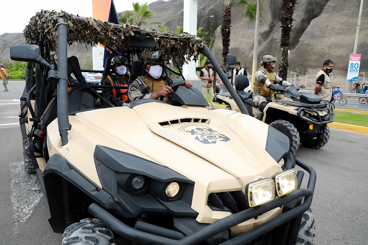 Masked Peruvian soldiers in camouflage drive an off-road patrol buggy along a coastal road in Lima, with another soldier on a quad bike behind
