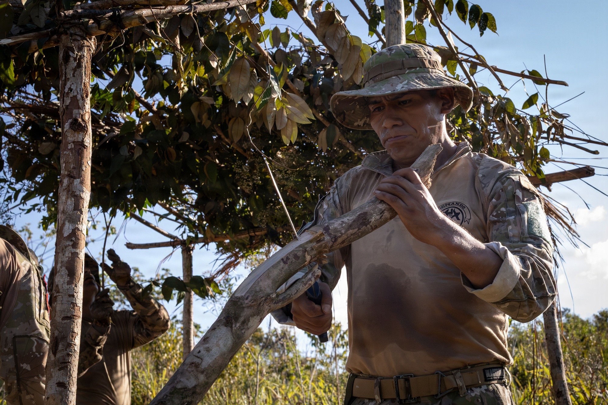 A Peruvian soldier in a bush hat cuts a branch to build a shelter during jungle training in Sauce, Peru