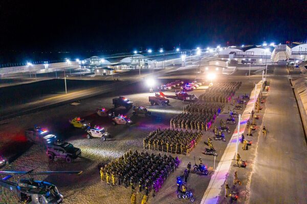 Night view of CECOT, El Salvador's mega-prison, with rows of security personnel, police vehicles and a helicopter assembled in front of white-roofed cell blocks