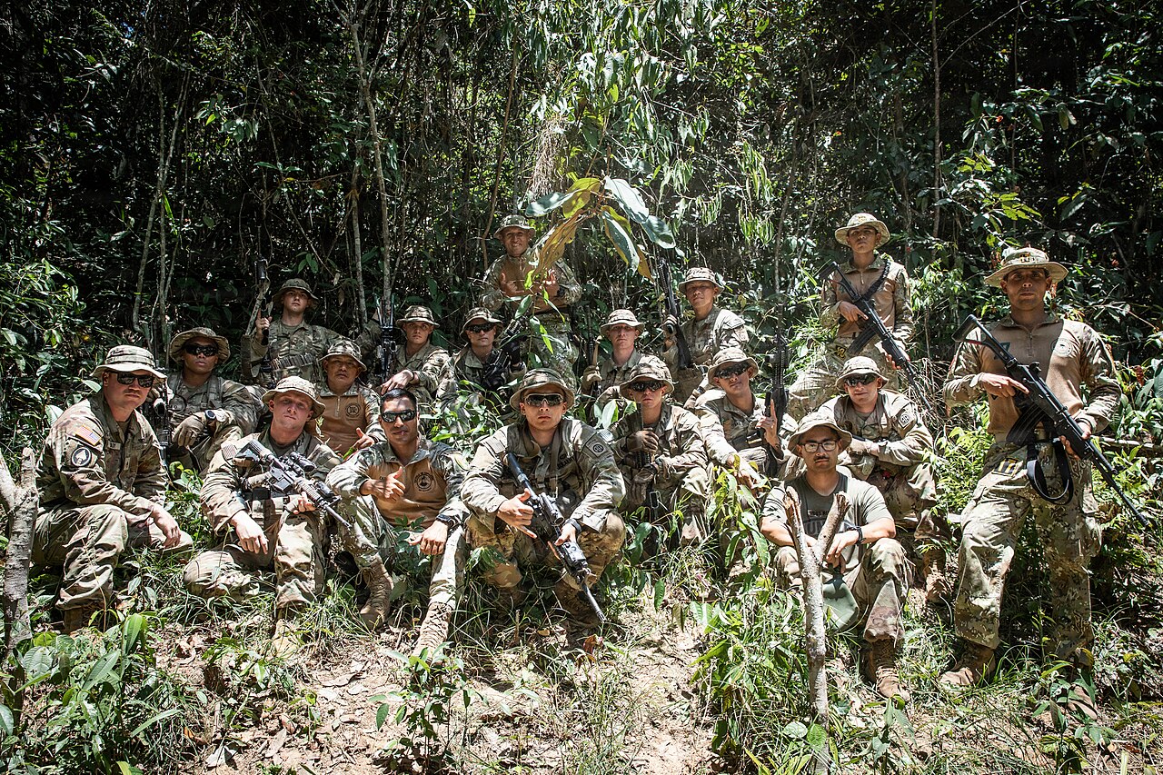 US soldiers and Peruvian jungle instructors in camouflage pose with rifles in dense Amazon forest