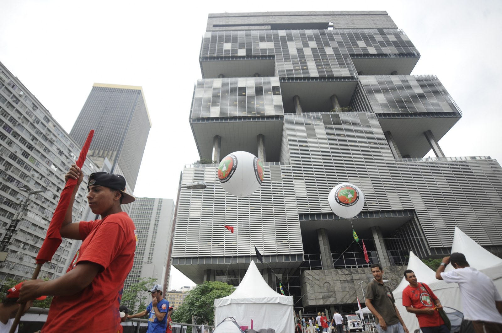 Tall stepped Petrobras headquarters tower in Rio de Janeiro with two large balloons and tents at its base during a demonstration