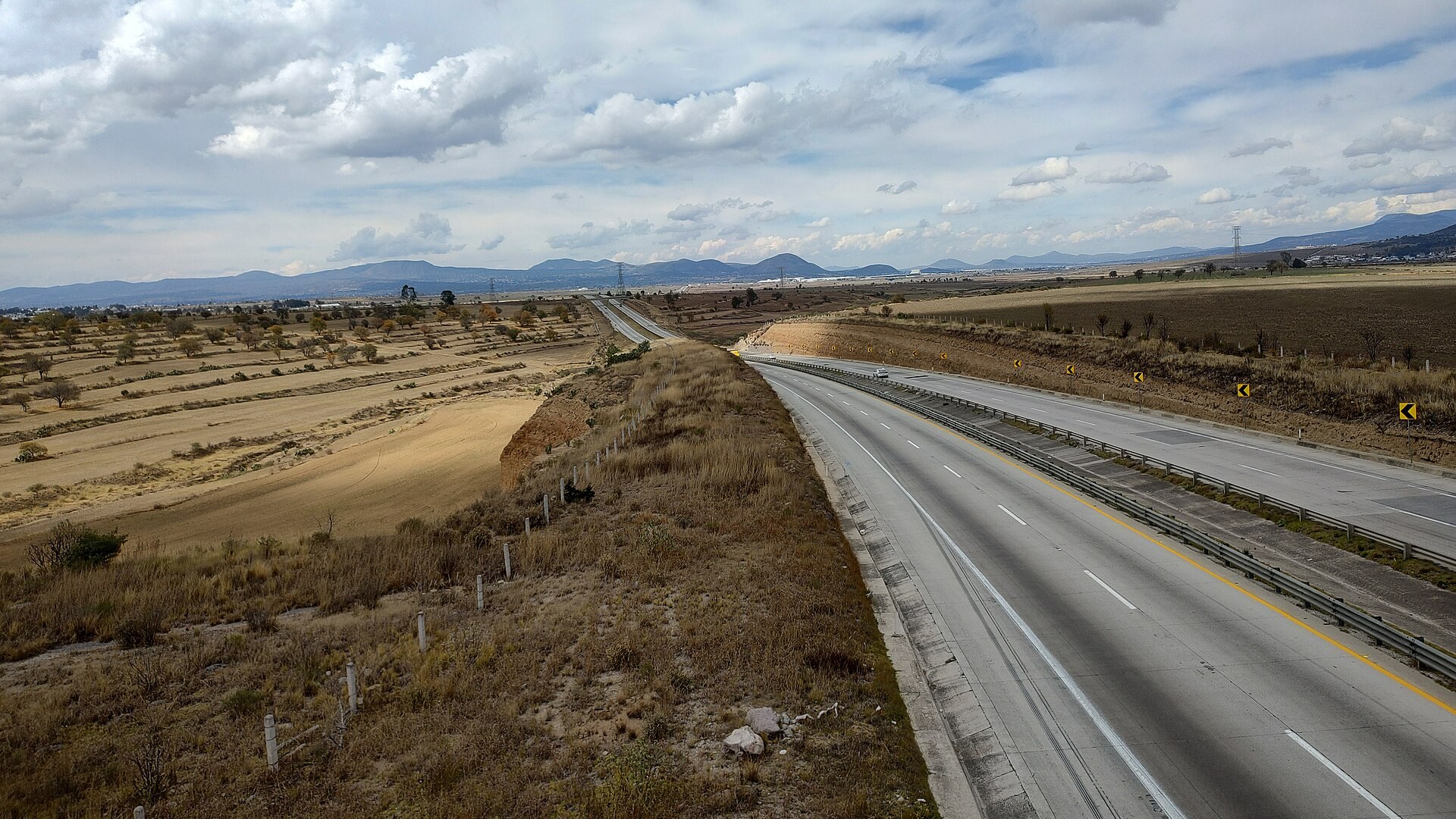 Toll motorway running through farmland under a cloudy sky near Sanctórum de Lázaro Cárdenas, Tlaxcala, Mexico
