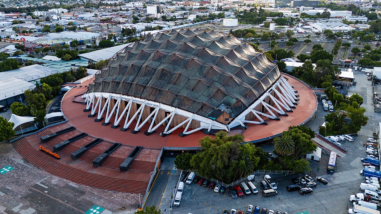 Aerial view of the domed Palacio de los Deportes arena in Mexico City with the entrance steps and a parking area.