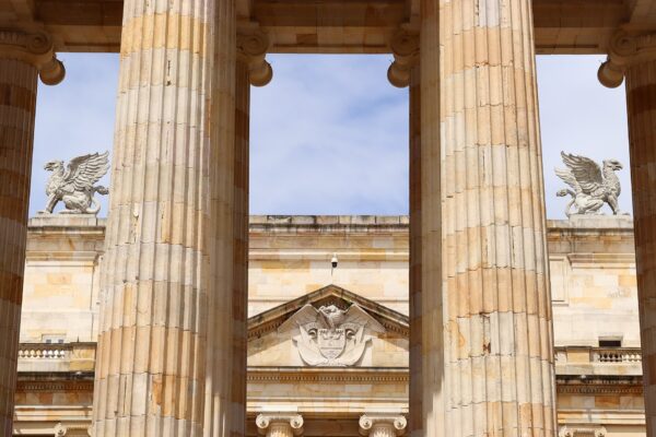 Sandstone columns of the Capitolio Nacional in Bogotá frame the building's pediment with Colombia's coat of arms and two griffin statues under a blue sky