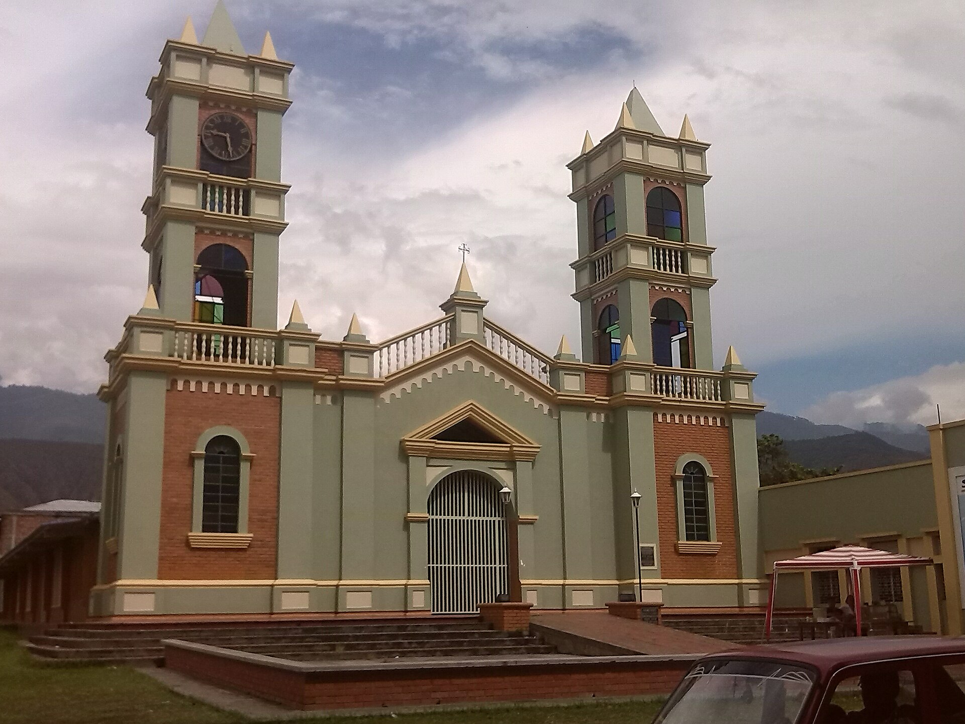 The pale green and brick church of Miranda, Cauca, with two bell towers, under a cloudy sky with mountains behind