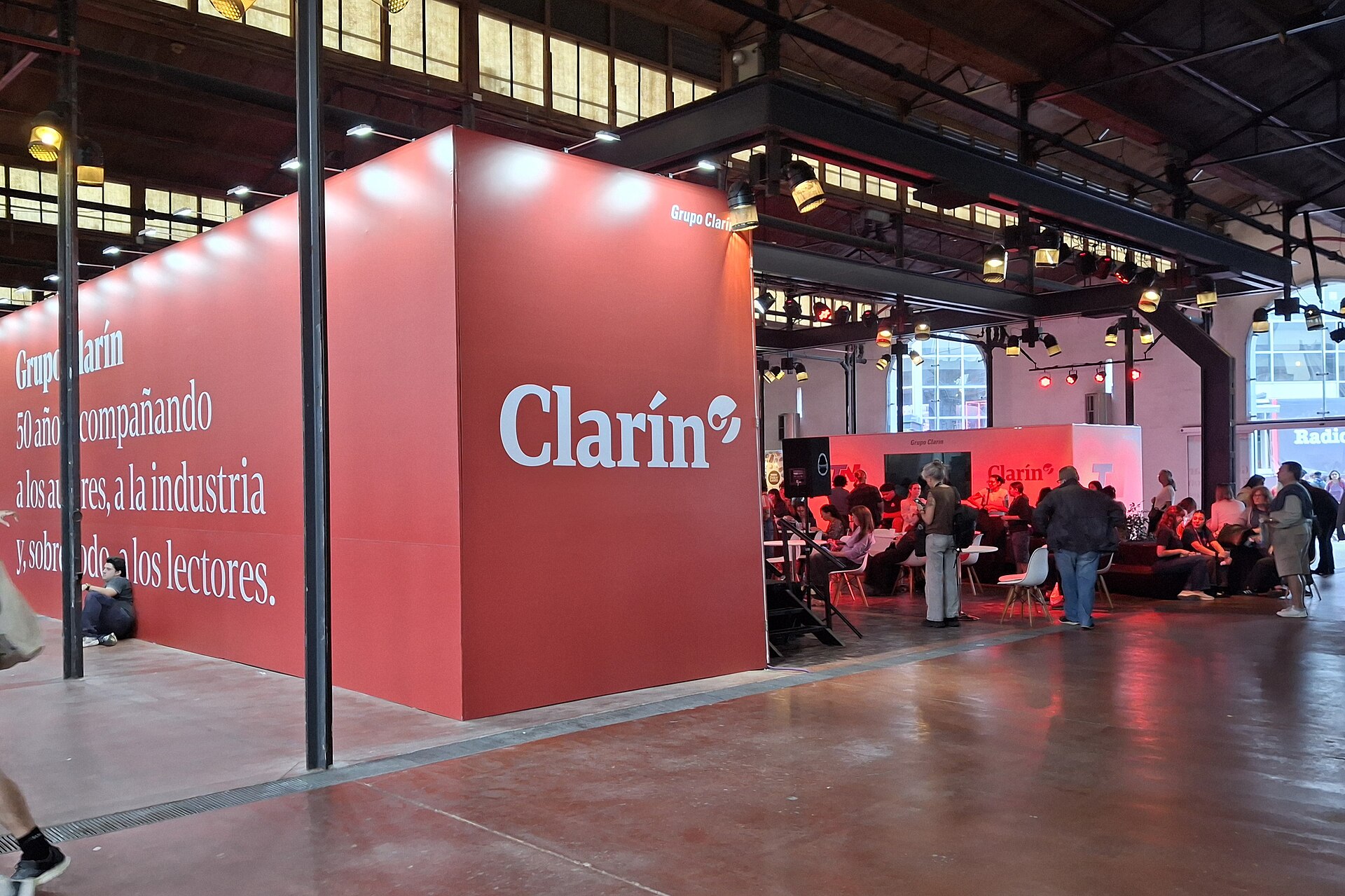 A large red Clarin-branded stand with visitors seated inside a hall of the Buenos Aires book fair