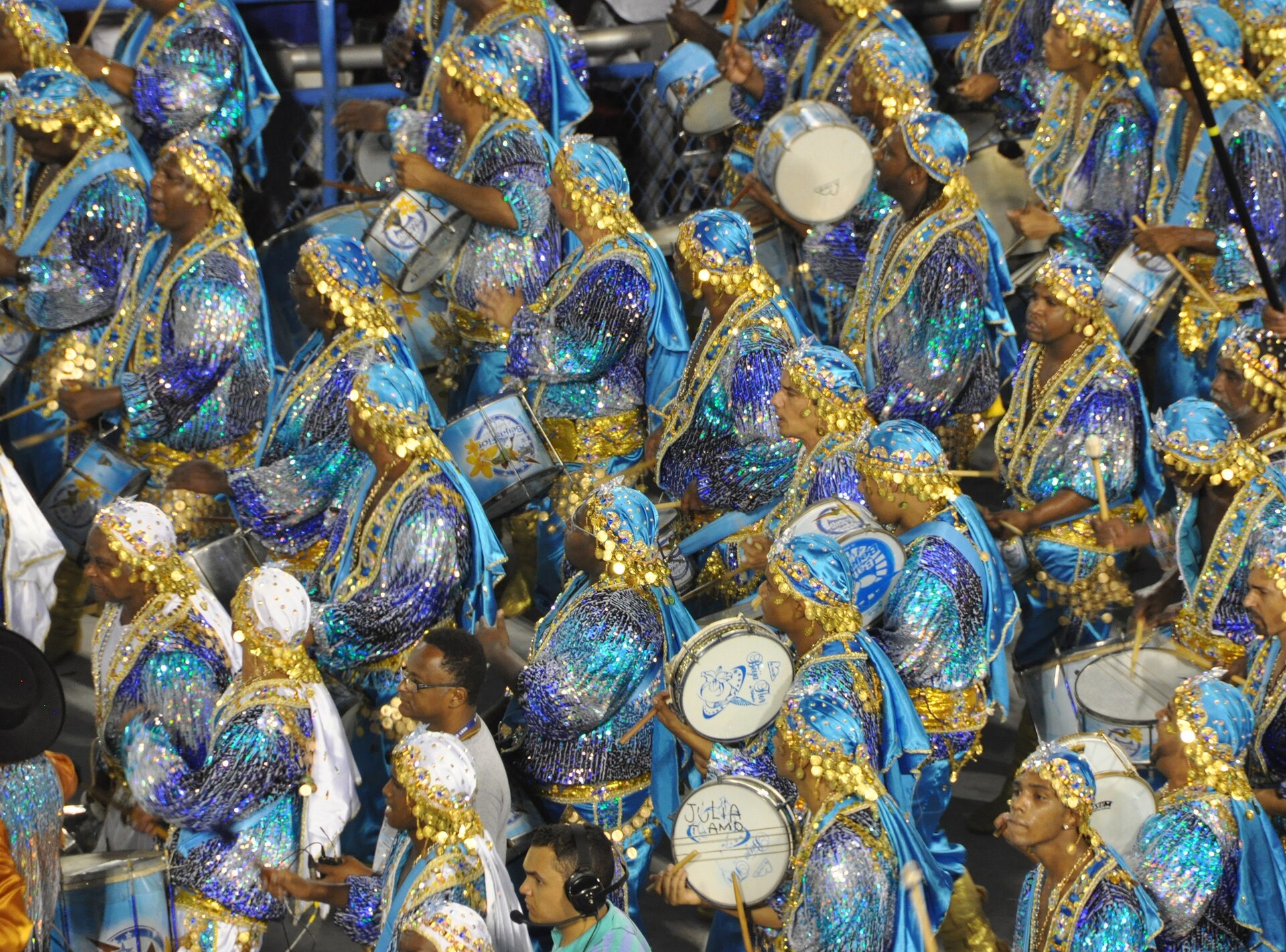 Drummers in blue and gold sequinned costumes playing white snare drums on the Sambadrome runway