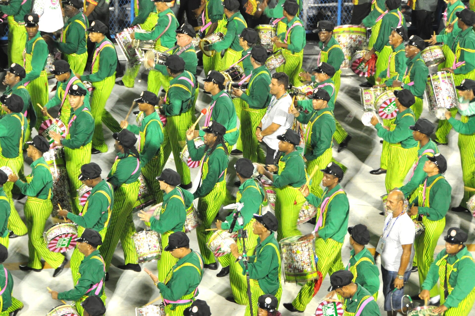 Drummers in green and pink striped costumes and black caps marching on the Sambadrome runway