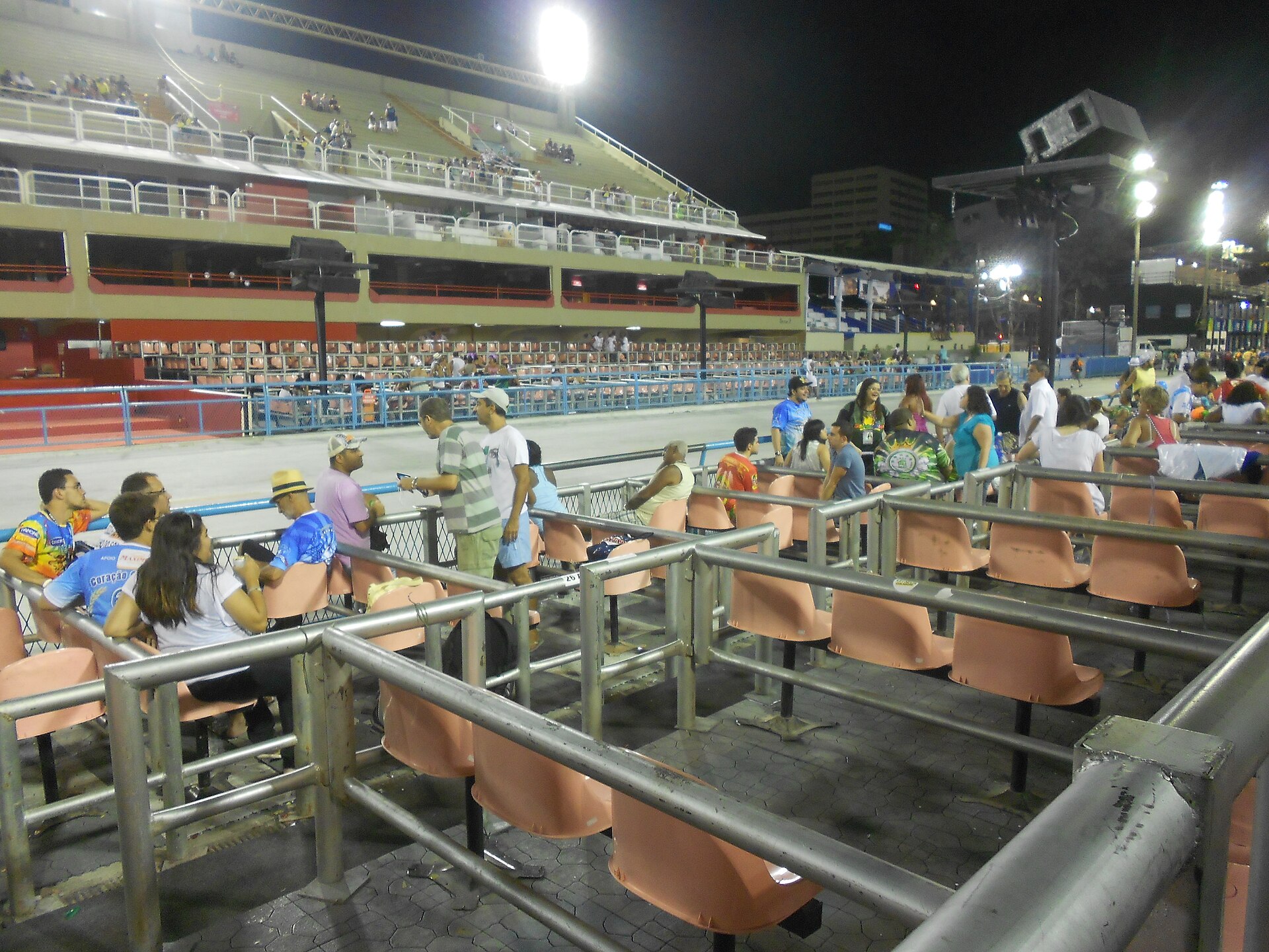 Salmon-coloured box seats and grandstands along the floodlit Sambadrome runway at night, with spectators taking their seats