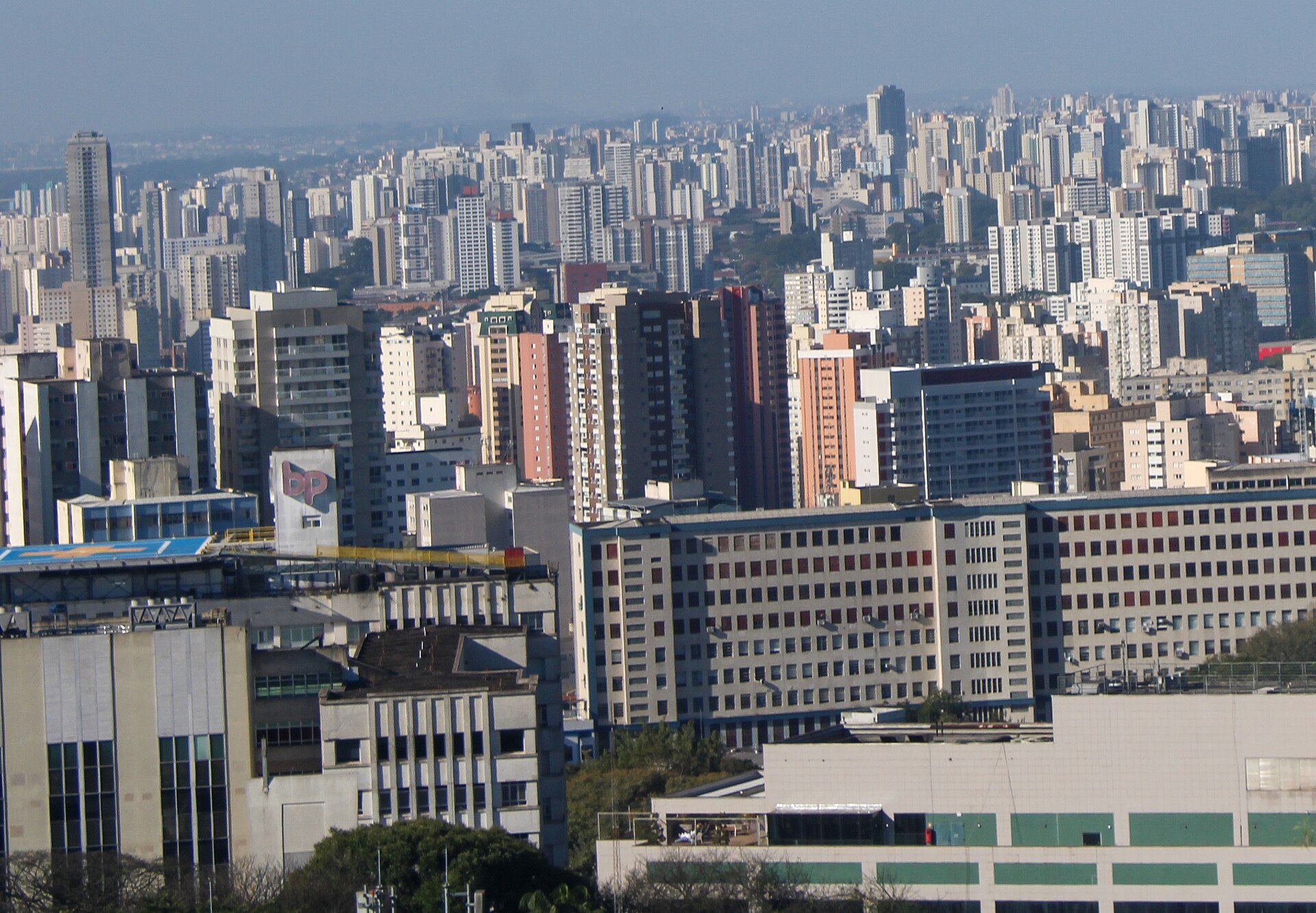 Dense rows of apartment and office towers stretch to the horizon under a hazy blue sky