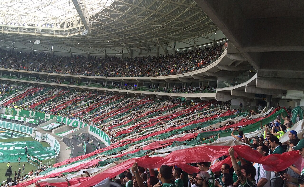 Palmeiras fans in a covered stand holding long red, white and green banners over the seats