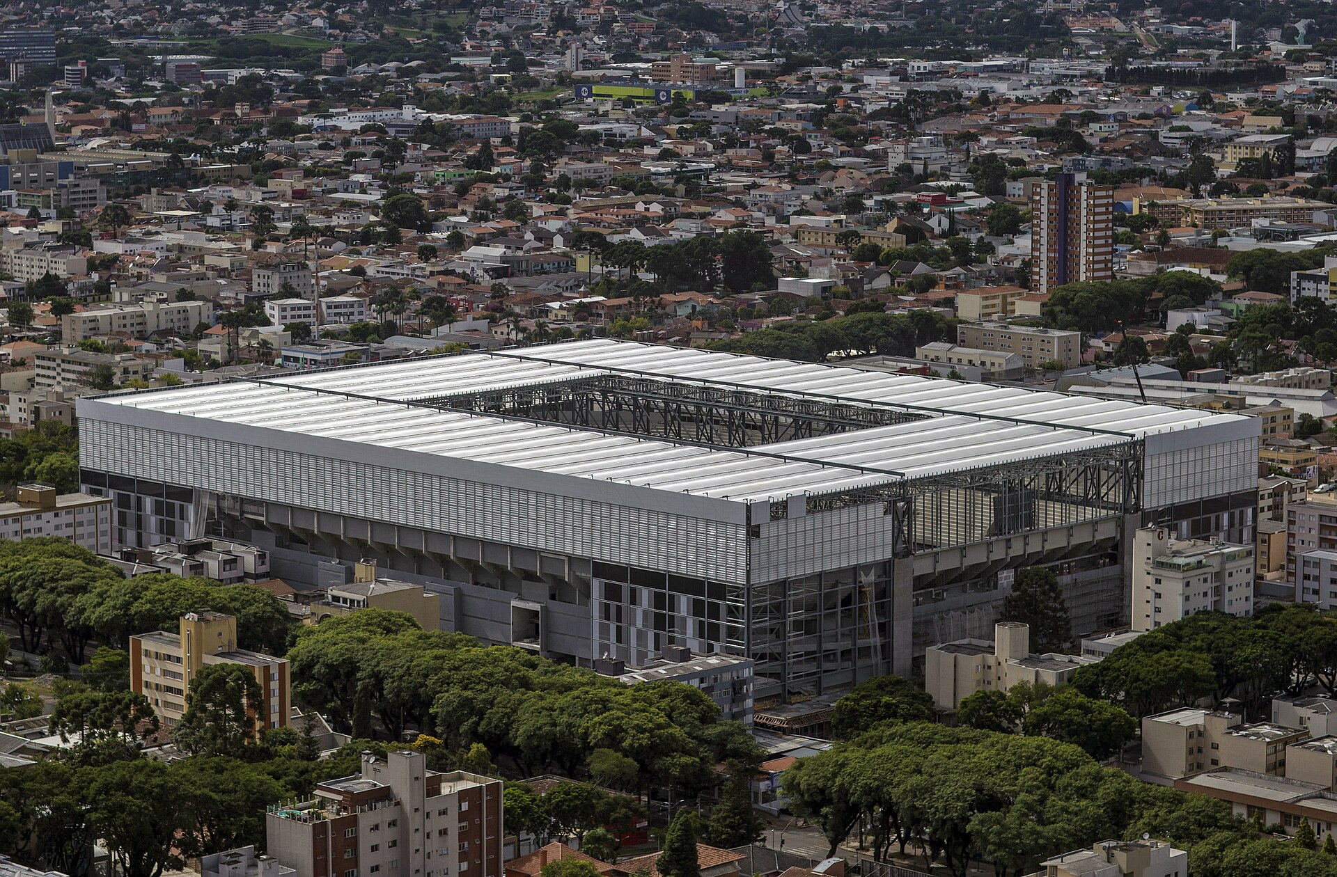 Aerial view of the boxy grey Arena da Baixada stadium surrounded by houses and trees in Curitiba