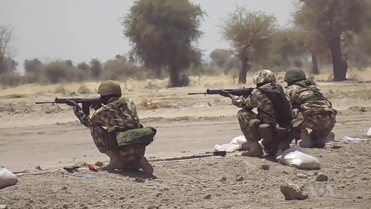 Nigerian Army soldiers kneeling with rifles at a firing line in dry bushland