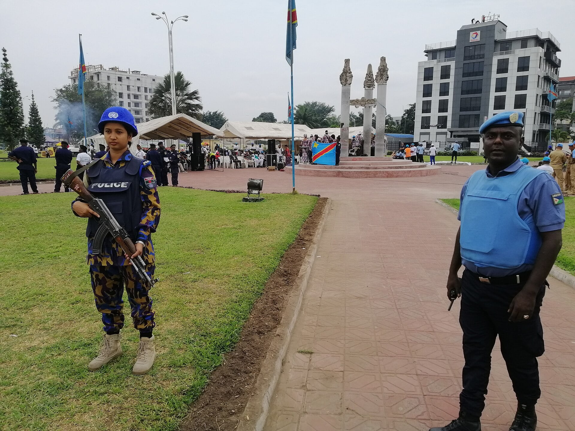 A woman police officer and a male UN police officer stand guard at a Peace Day event in Kinshasa with the Congolese flag behind them