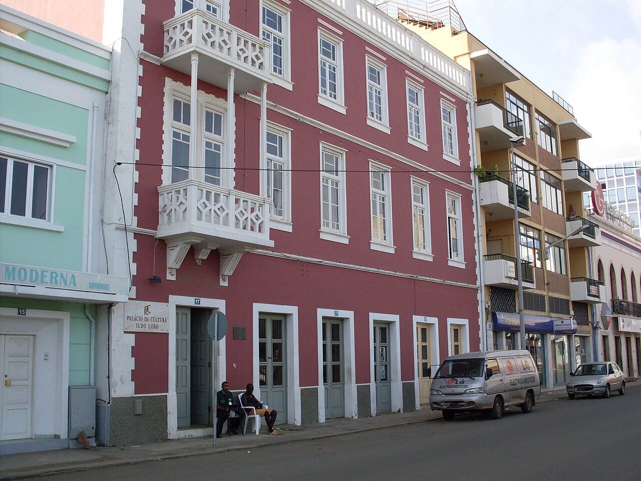 The red-painted Palácio da Cultura Ildo Lobo, a colonial-style building with white balconies, on a street in Praia
