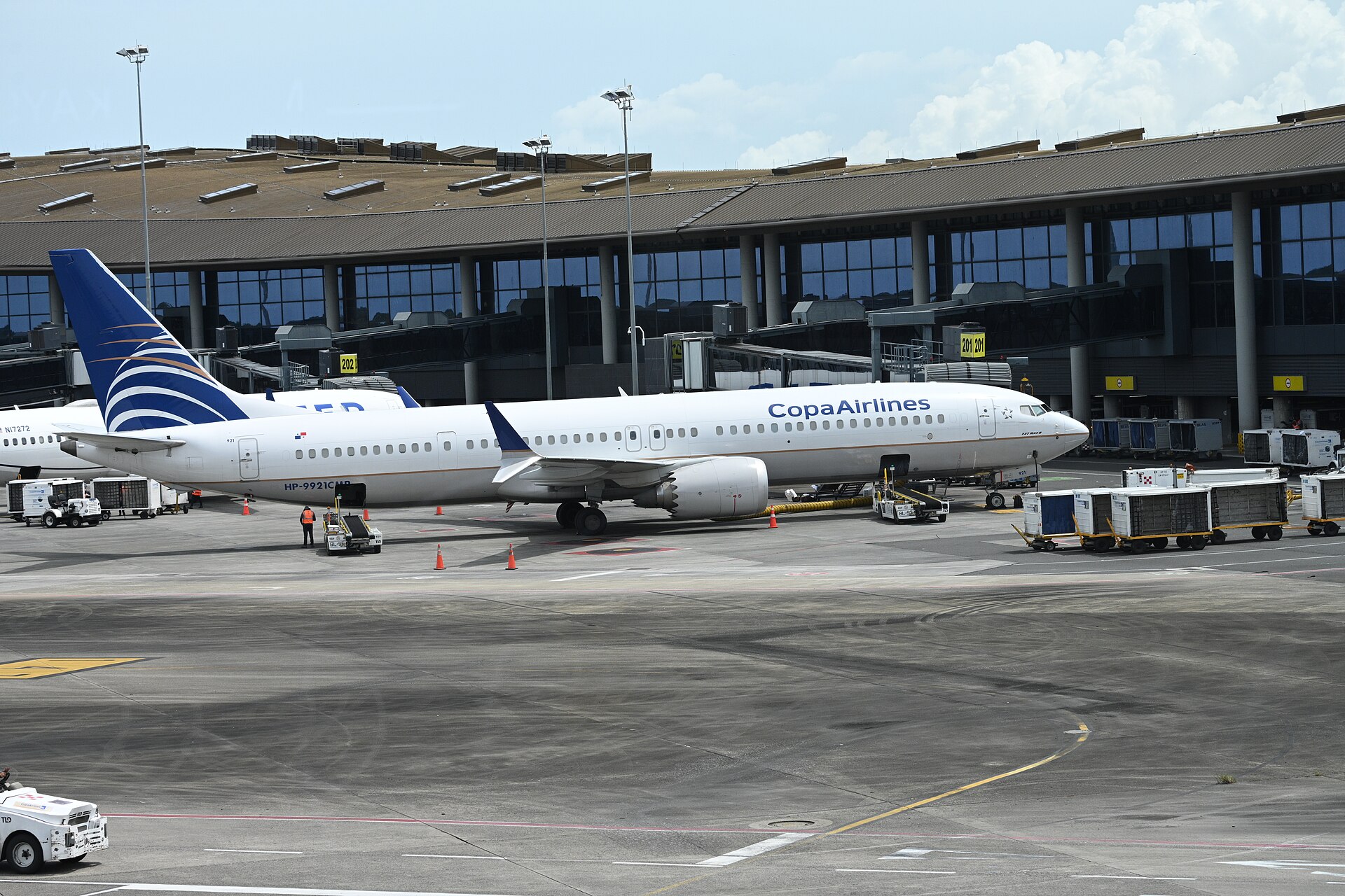 A white Copa Airlines Boeing 737 with a blue tail parked at a gate of Tocumen International Airport's glass-fronted terminal, with baggage carts on the apron