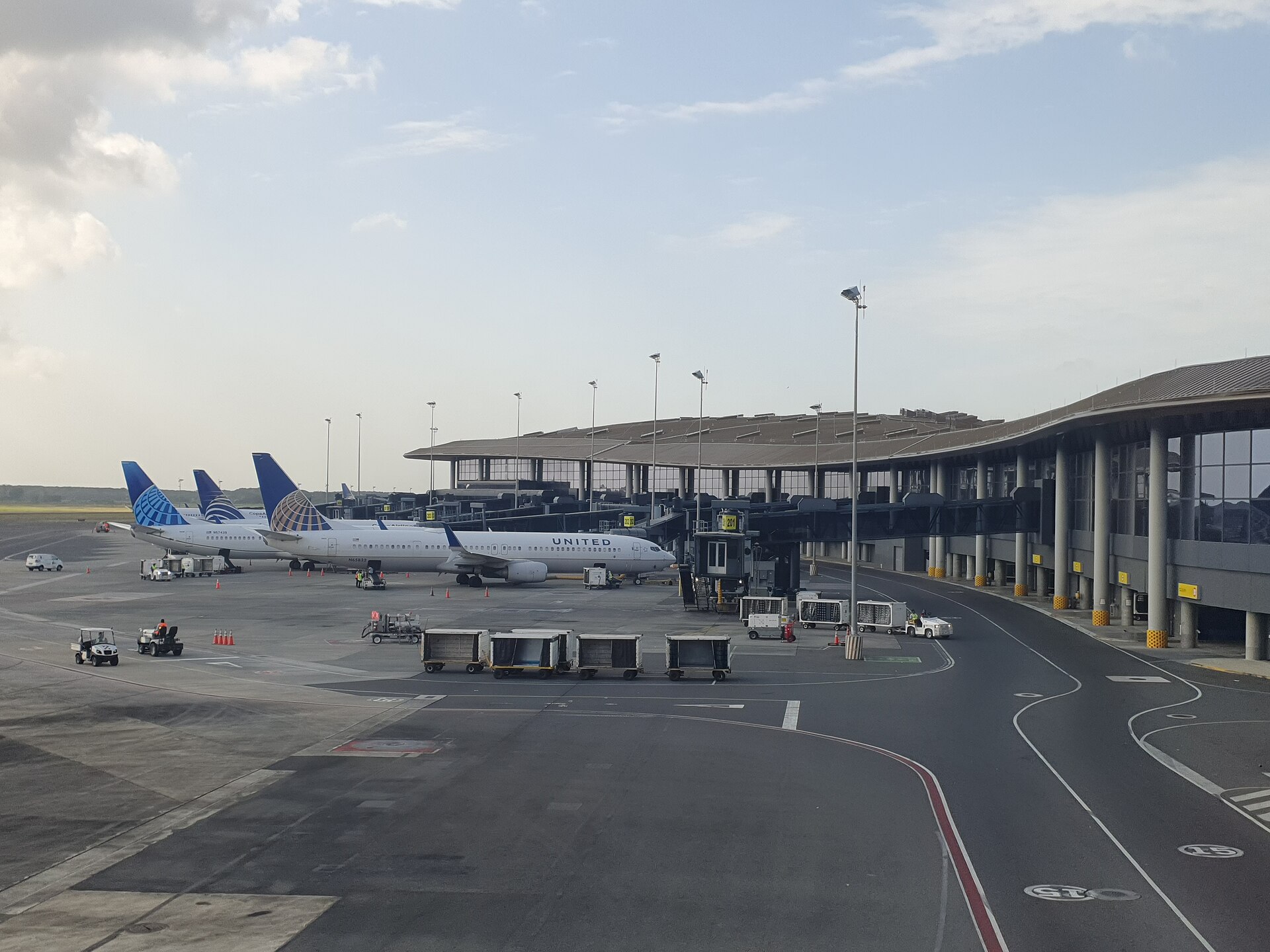 Three United Airlines jets parked at gates of the curved Terminal 2 building at Tocumen International Airport, with baggage carts on the apron under a cloudy sky