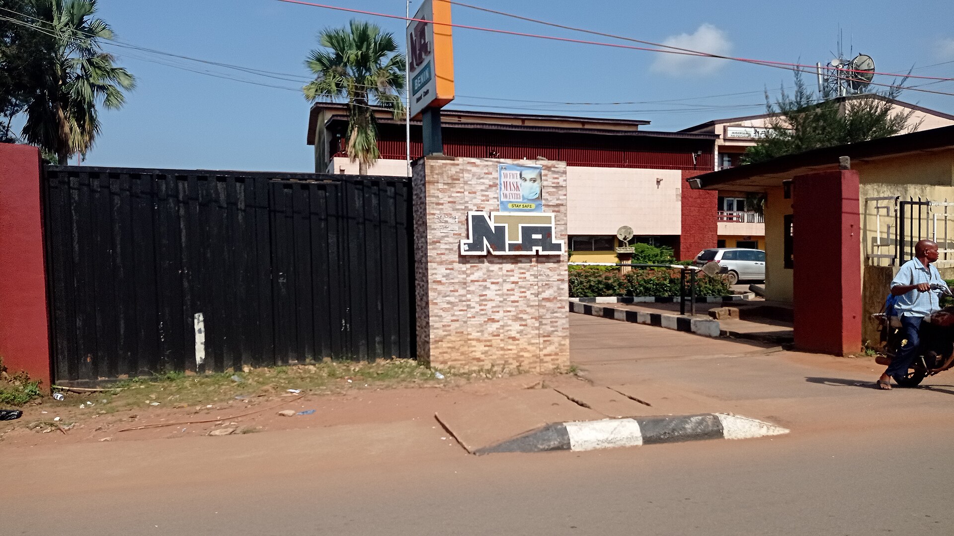 Gate and sign of the Nigerian Television Authority station in Benin City with a motorcyclist passing