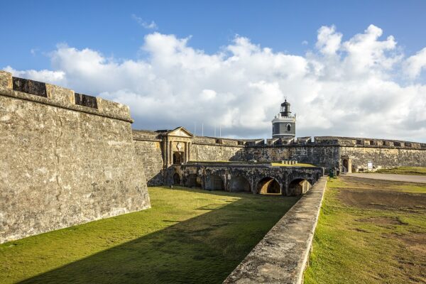 The stone walls and arched bridge of the Castillo San Felipe del Morro fortress in Old San Juan, with its grey lighthouse under a blue sky