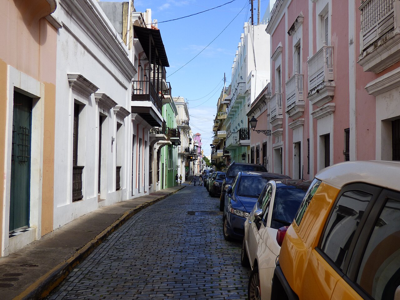 A cobbled street in Old San Juan lined with pastel-coloured colonial houses with balconies and parked cars